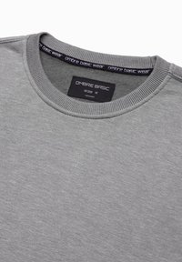 Grijze sweatshirt met geribde ronde hals en zachte textuur. Etiket met "OMBRE BASIC" en maat "M" zichtbaar binnenin de kraag.