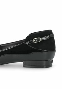 Des ballerines noires en vernis et en daim présentent un design élégant, un petit talon carré et une sangle ajustable avec un détail de boucle en argent.