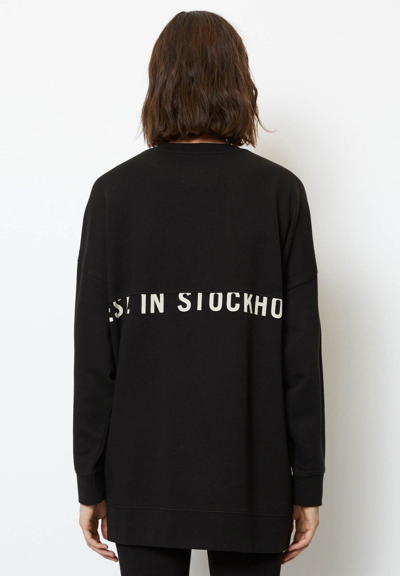 Sudadera negra hecha de material suave, con un corte relajado. Incluye el texto blanco "EST. EN ESTOCOLMO" en la parte trasera. Mangas largas, puños acanalados.