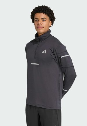 Sudadera gris oscuro con medio cierre, mangas largas, acentos reflectantes, textura acanalada y logotipo bordado en el pecho y el bolsillo de la manga.