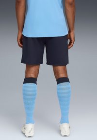 Maillot de sport bleu, shorts navy et chaussettes rayées bleues. Les chaussettes présentent un design texturé et une bande sombre unie en haut. Chaussures à crampons blanches.