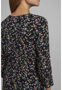 Robe à motif floral avec un fond bleu marine, présentant de petites fleurs multicolores, des manches longues et une coupe décontractée. Tissu texturé.