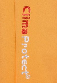Oranssi kangas, jossa on brodeerattu teksti "Clima Protect" punaisella ja valkoisella ompellulla, joka näkyy tekstuuripinnassa ja kankaan kudontarakenteessa.