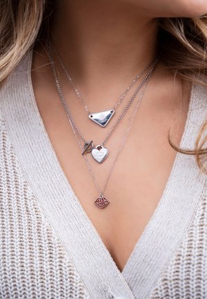 Trzy warstwowe srebrne naszyjniki: zawieszki w kształcie trójkąta, serca i wargi. Teksturowane łańcuszki o różnych kształtach i grawerowanych detalach.