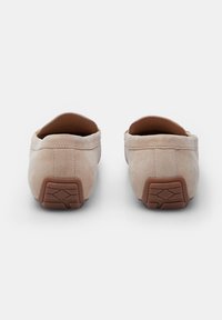 Beige mokkasiner i ruskind med flad brun gummisål, der har lav hæl og enkel syning for forbedret komfort.
