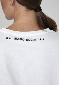 Witte t-shirt met een ronde halslijn en korte mouwen. Zwarte tekst "MARC ELLIS" met twee sterren gedrukt op de bovenrug. Zachte katoenstof.