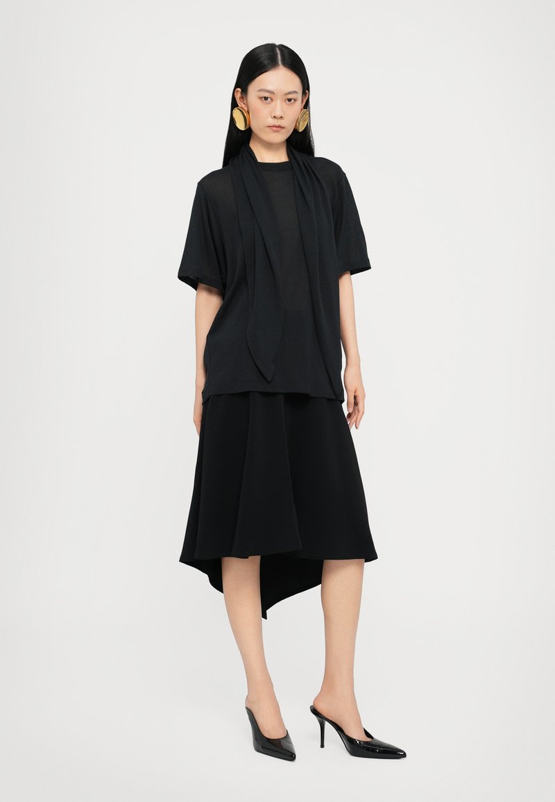 Black ensemble featuring a short-sleeve top with draped front and asymmetrical hem skirt. Worn with pointed black heels.