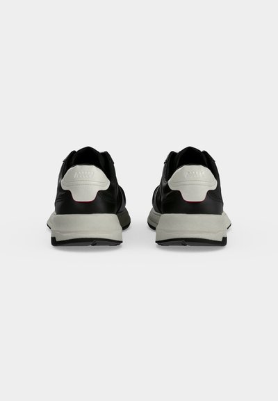 Paire de baskets noires et blanches vues de dos, avec des semelles blanches épaisses et des semelles extérieures noires sur un fond uni.