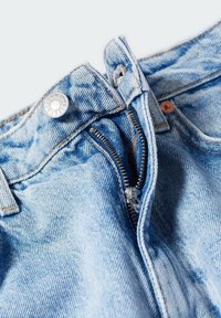Jean en denim bleu clair avec une fermeture éclair argentée ouverte et un bouton métallique sur la ceinture, sur un fond uni.