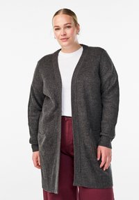 Tmavo šedý rebrovaný cardigan s dlhými rukávmi, otvoreným frontom a dvoma prednými vreckami, skombinovaný s bielym topom a bordovými nohavicami.