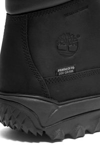 Schwarzer wasserdichter Stiefel mit einem glatten Lederoberteil und gesteppten Akzenten sowie einer robusten, strukturierten Sohle. Das Etikett weist auf Primaloft-Isolierung hin.