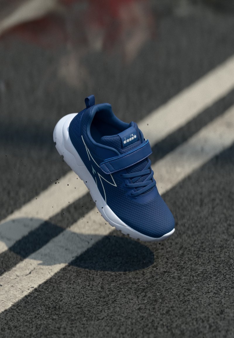 Chaussure de sport bleue avec un dessus en mesh, semelle blanche, bande réglable et lacets ; présente des accents blancs diagonaux sur le côté.