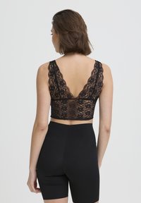 Bralette en dentelle noire avec un dos en V et des bords festonnés, présentant des motifs floraux et une longueur courte, associé à un short noir taille haute.