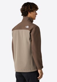 Tan ja brown takki, jossa on korkea kaulus, takana logo, valmistettu sileästä kankaasta, jossa on kontrastivärinen yläosa.