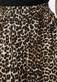 Lapas druku svārki ar savelkamu, elastīgu jostasvietu, kas veidoti ar melnu, brūnu un baltu krāsu kombināciju gludā auduma tekstūrā.