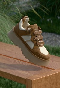 Brune og kremfargede sneakers med en chunky såle, teksturerte materialer og snøring. Har en bakre løftestrop og subtil merking på siden.
