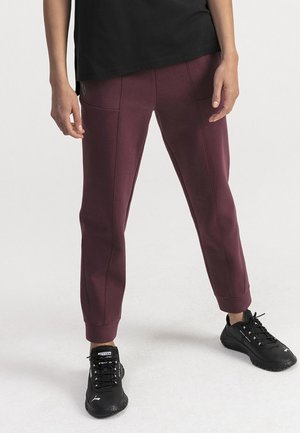 Pantalons de jogging bordeaux en tissu doux, dotés de poches avant, de poignets côtelés et de détails de couture contrastants. Portés avec des baskets noires.
