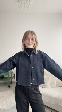 Μαύρο τζιν μπουφάν με κουμπιά, χαρακτηριστικά με λευκές βούλες, άνετη γραμμή, φαρδιά μανίκια και κοντό σχέδιο, συνδυασμένο με μαύρο παντελόνι.