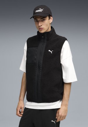Black fleece vest with zip closure and a chest pocket, worn over a white t-shirt. Black baseball cap featuring a white Puma logo.