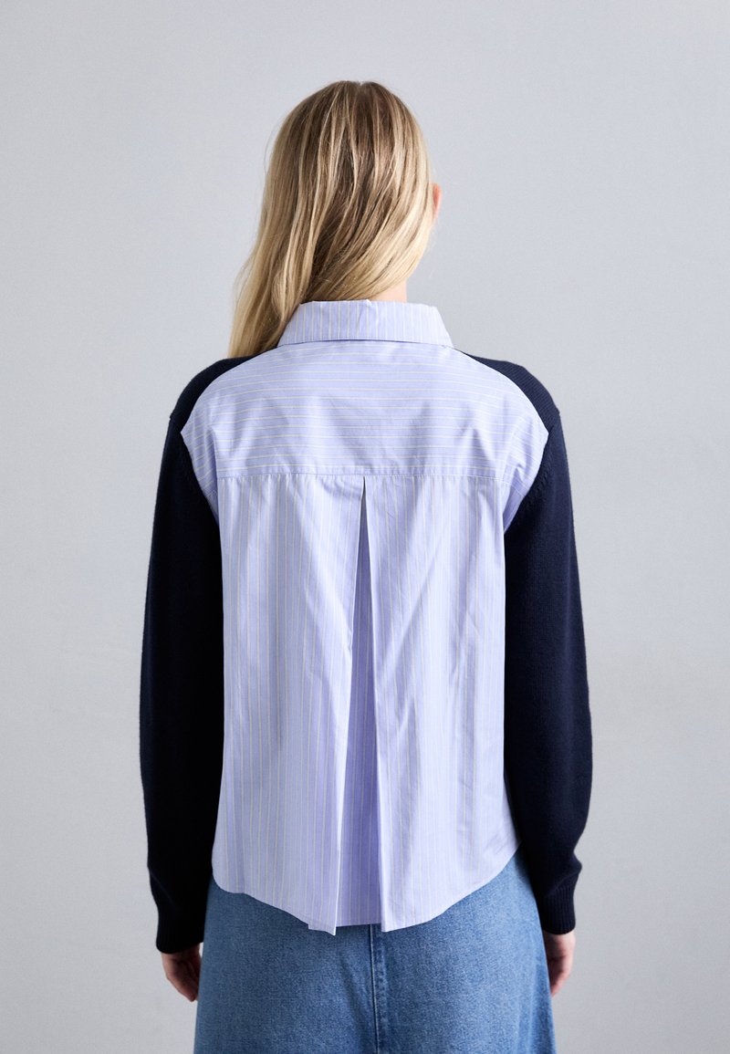 Camicia con schiena in cotone a righe azzurre chiare e maniche lunghe blu navy, con una piega al centro e un colletto classico.