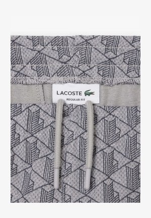 Joggers en tissu gris texturé avec un motif géométrique, une ceinture élastique avec cordon de serrage, et une étiquette indiquant "LACOSTE REGULAR FIT".