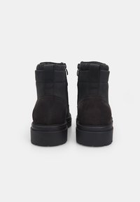 Botas negras hasta el tobillo con acabado de ante, cuello de tela texturizada y suela de goma. Incluyen cremalleras laterales y costuras reforzadas.