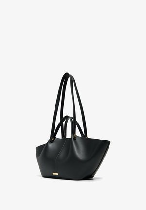 Sac fourre-tout en cuir noir avec deux longues bandoulières et deux poignées plus courtes, en forme de trapèze, avec une plaque de marque en ton doré sur le devant.