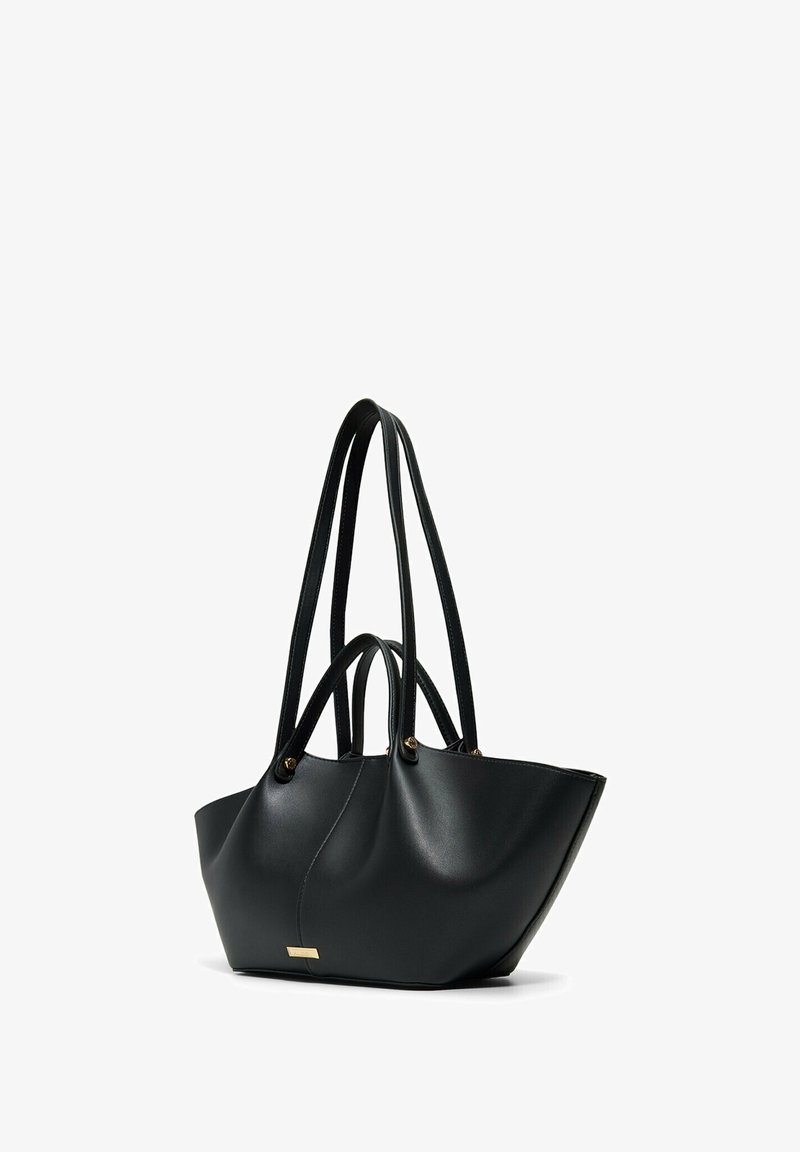 Czarna skórzana torba tote z dwoma długimi paskami na ramię i dwoma krótszymi uchwytami, w kształcie trapezu, złocona plakietka z logo z przodu.