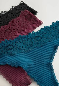 Drie paar dames string ondergoed met kant afgewerkt in zwart, bordeauxrood en teal. De stof heeft een geribbelde textuur en bloemkant accenten.