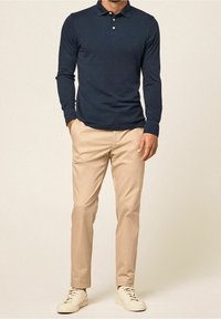 Marineblaues Langarm-Polohemd mit Kragen, kombiniert mit beigen Chinos und weißen Sneakers. Einfaches Design mit Knopf-Details.