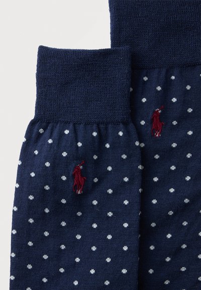Deux chaussettes bleu marine à pois blancs avec un petit logo brodé d’un joueur de polo rouge sur chacune.
