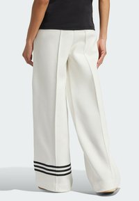 Szerokie, białe spodnie z fałdami z przodu, czarnymi paskami na brzegu i gładką fakturą. Zaprojektowane z myślą o komforcie i luźnym kroju.