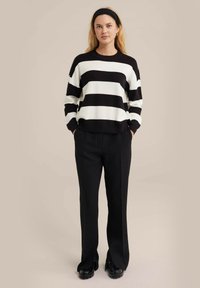 Mustvalge triibuline sviiter ümarate kaelustega, lopsakas, pikkade varrukatega, koos mustade laiade pükstega ja tikk-kontsadega mustade kingadega.