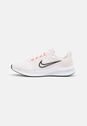 Chaussure de course Nike rose clair avec logo Swoosh noir, semelle blanche et tige en mesh, vue de côté sur fond blanc.