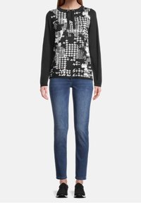 Svart långärmad topp med ett vitt abstrakt mönster, rund halsringning och stängning med två knappar; matchad med blå jeans och svarta sneakers.