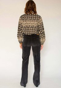 Pantalons évasés en velours côtelé noir associés à un chemisier à manches longues à motifs présentant des designs abstraits en beige et noir.