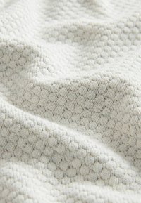 Tissu texturé dans un motif ondulé, présentant une couleur gris clair avec une apparence tissée douce et des formes hexagonales légèrement surélevées.