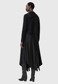 Μαύρος, ριγωτός πλεκτός σλίπ με φαρδύ γιακά, συνδυασμένος με μια ρο流ιά, πλισέ μαύρη φούστα και ψηλοτάκουνες μαύρες μπότες.