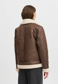 Veste en cuir marron avec un col et des poignets en shearling crème, dotée d'une coupe droite et de détails de couture subtils.