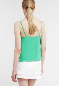 Zelená hedvábná tílka s tenkými ramínky, volného střihu a hladké textury. Nosená s bílou strukturovanou mini sukní.