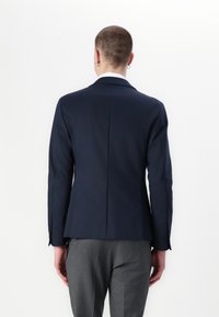 Navy blazer with a tailored fit, featuring a single vent, smooth texture, and styled with gray trousers. Back view highlights a clean design.