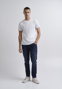 Camiseta blanca de manga corta, vaqueros azules y zapatillas blancas. La camiseta tiene cuello redondo; los vaqueros son ajustados y ligeramente desgastados.