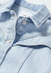 Hellblaue Jeansjacke mit klassischem Kragen, silbernen Druckknöpfen und sichtbaren Nähten. Etiketten sind im Kragen eingenäht.