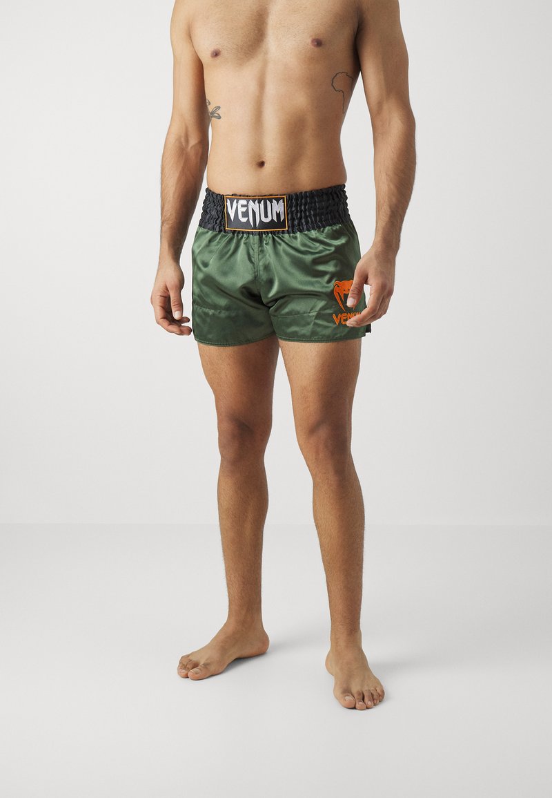 Calções de boxe verde em satin com faixa elástica na cintura. Apresenta o logótipo "VENUM" em preto na faixa e o logótipo laranja no lado esquerdo.