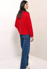 Felpa rossa con collo alto e maniche lunghe, abbinata a jeans blu a gamba larga. Design semplice e texture morbida.
