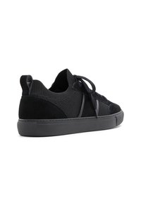 Zapatilla negra con parte superior de punto y acentos de ante, puntera redonda, suela de goma plana y cierre con cordones. Los materiales texturizados ofrecen contraste.