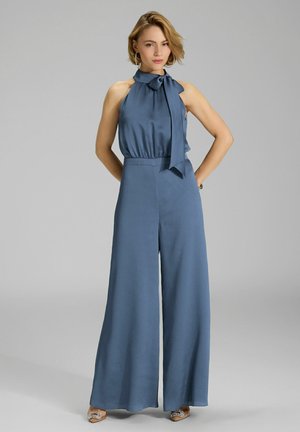 Combinaison bleu à halter avec détail nœud au cou, tissu texturé, design à jambes larges et talons strappy décorés.