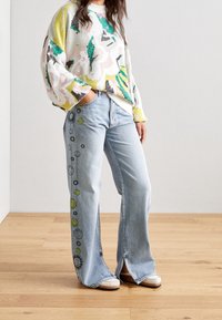 Suéter multicolorido de punto con patrones florales; jeans de pierna ancha azul claro con diseños de sol y cara sonriente en el costado.