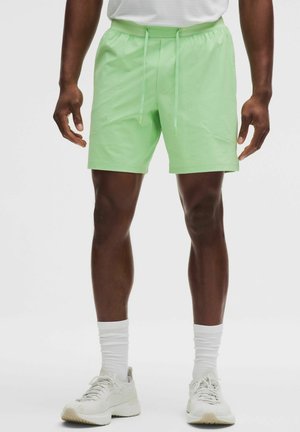 Mann trägt hellgrüne Shorts mit Kordelzug, weiße Socken und weiße Turnschuhe und steht mit entspannten Händen.