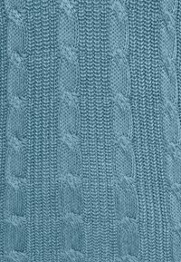 Tissu tricoté bleu avec un motif texturé de câbles tressés verticaux et de mailles côtelées.